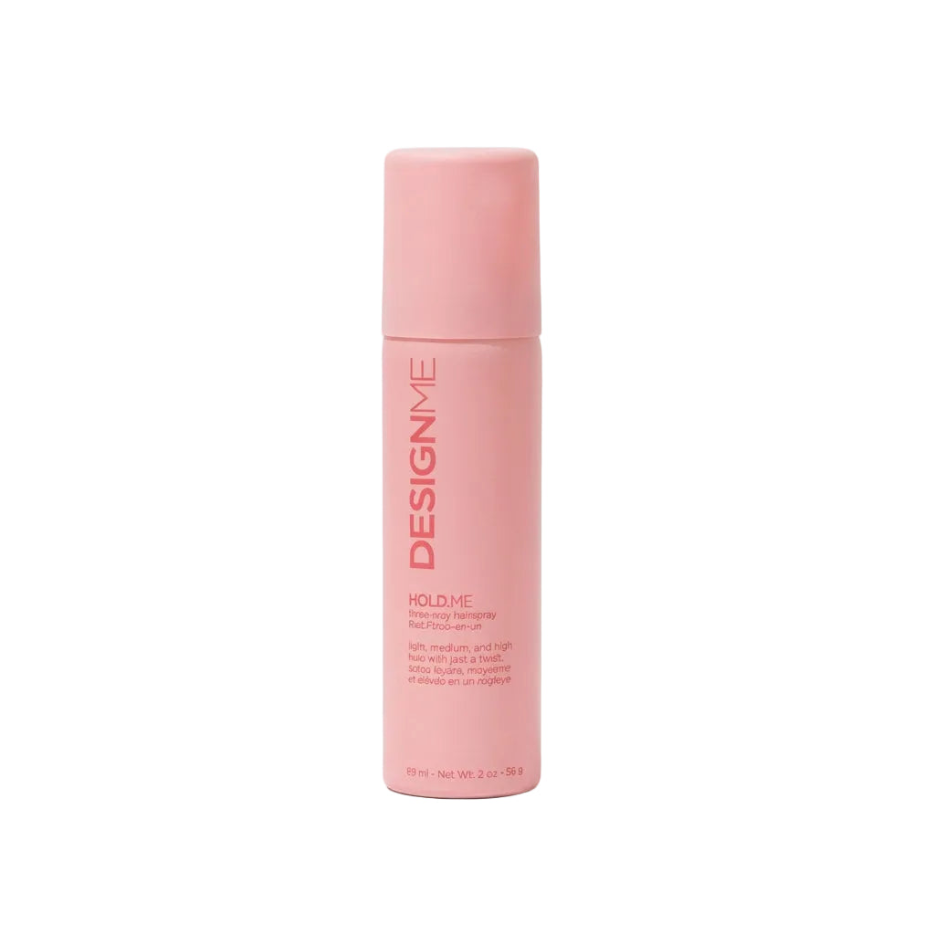 A pink cylindrical bottle of DesignMe Hold Me hair product, standing upright on a clean white background with a soft shadow.